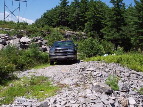 2001 Ford Crown Victoria - A dark pickup truck is parked on a rough gravel road amidst a rocky, wooded landscape.