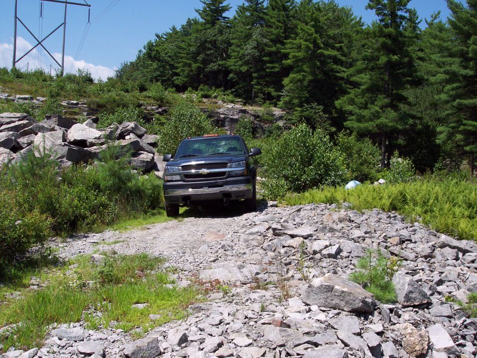 Dark pickup truck on a gravel road surrounded by rocks and trees