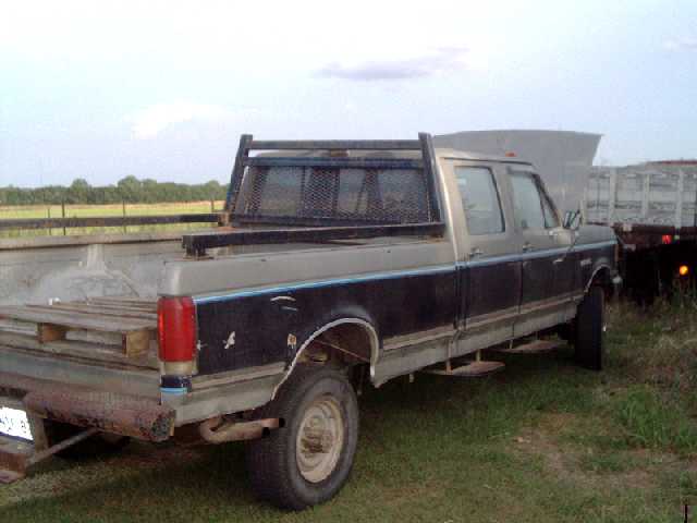 Two-tone Ford crew cab dually pickup with headache rack parked in a grassy field