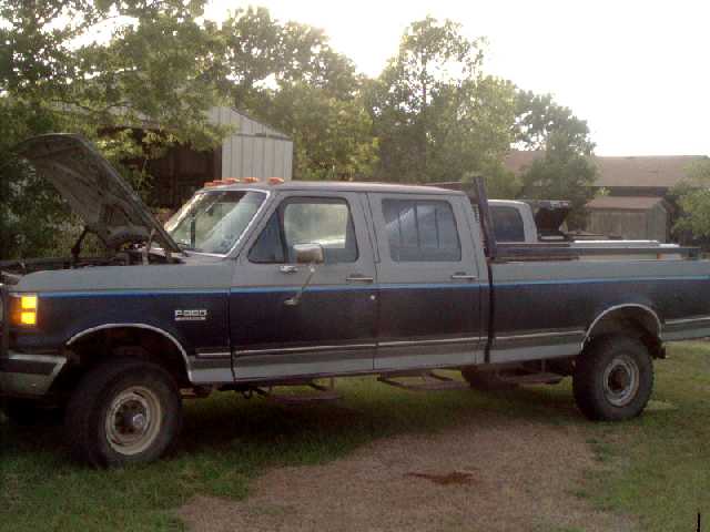 Blue and gray Ford F-350 crew cab pickup with hood up parked on grass