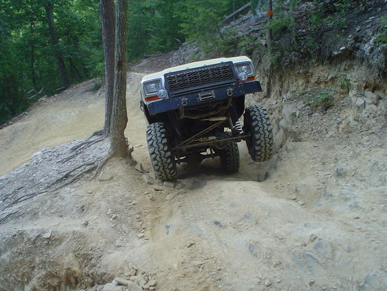 White off-road vehicle with large tires climbing a rocky incline