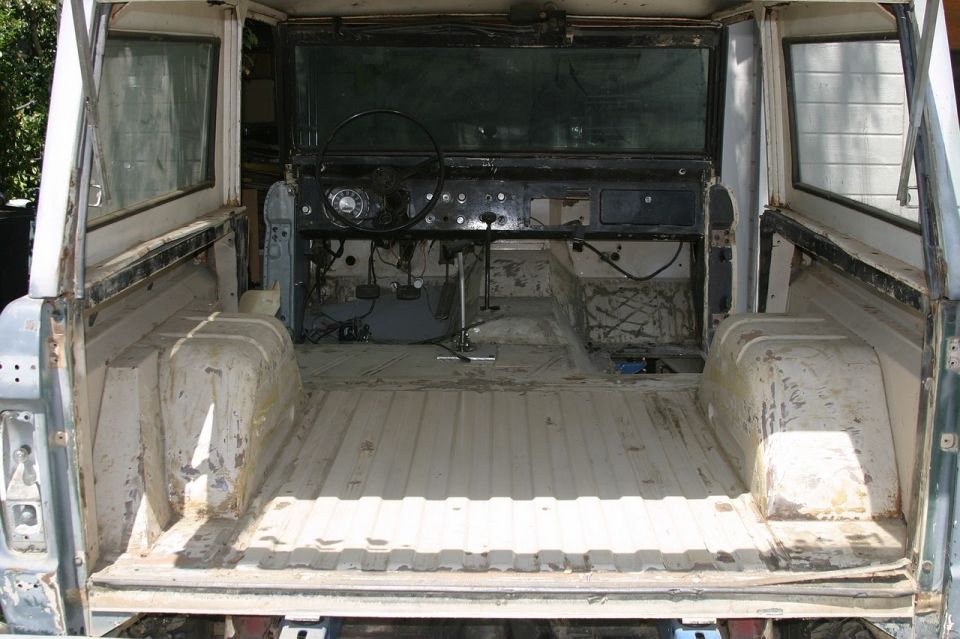 Gutted early Bronco interior from the tailgate showing bare floor pan, dash and steering wheel