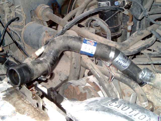 New black upper radiator hose with clamps and blue label resting in a dusty truck engine bay