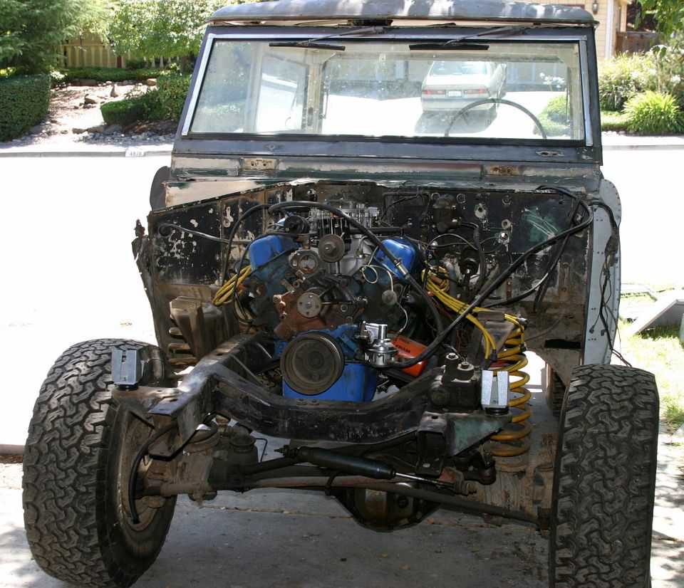 Front view of a classic Ford Bronco, engine bay is open and engine is removed, showing the chassis and suspension components