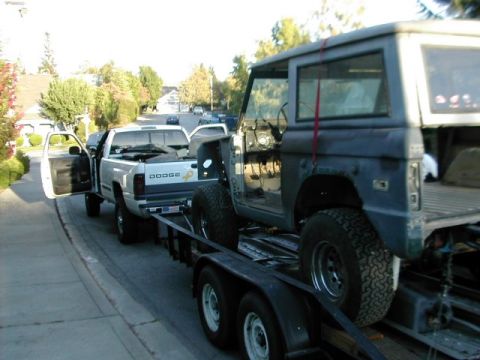 1971 Ford Bronco - A gray 1971 Ford Bronco is loaded onto a trailer towed by a white Dodge pickup truck.