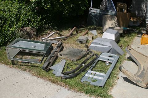 1971 Ford Bronco - Various disassembled vehicle parts are laid out on the grass, including a door, exhaust system, and fender.