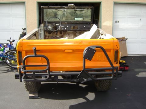 1971 Ford Bronco - The rear of a classic Ford Bronco, painted orange, is shown with custom off-road bumpers and a spare tire mount.