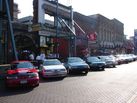 1992 Ford Taurus - A line of Ford Tauruses are parked on a brick street in front of historic buildings.