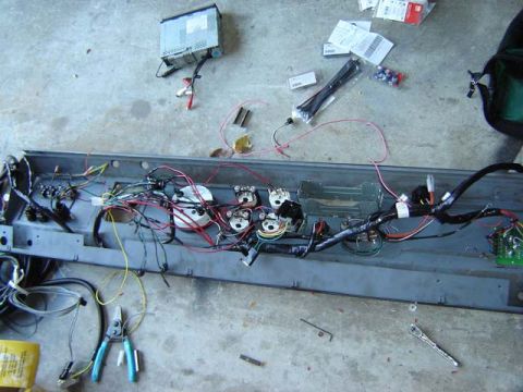 1971 Ford Bronco - Disassembled dashboard wiring harness with gauges and radio removed, lying on a concrete floor with tools and parts.