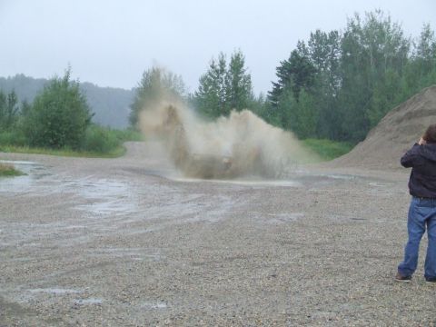 1990 Ford Bronco - A vehicle creates a large splash as it drives through a muddy area, with a person watching in the foreground.