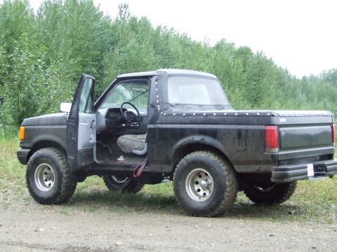 1990 Ford Bronco - 1990 Ford Bronco with soft top and open driver's door, parked off-road.