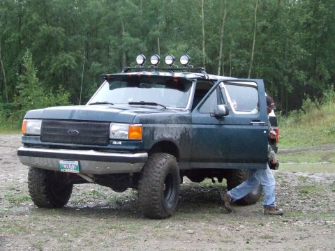 1990 Ford Bronco - A person exits a green 1990 Ford Bronco with off-road modifications.