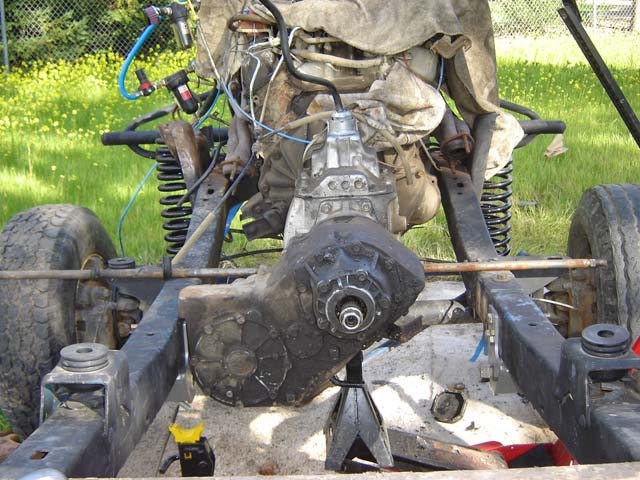 Stripped frame on jack stands showing transmission, transfer case and crossmember