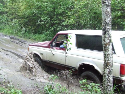 1990 Ford Bronco - Ford Bronco navigating a difficult muddy path in a wooded area.