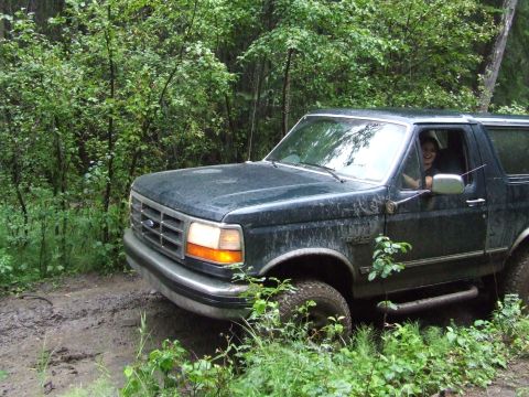 1990 Ford Bronco - 1990 Ford Bronco navigating a wet, wooded trail with a person driving.