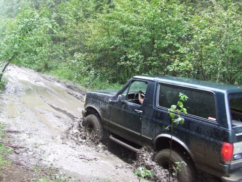 1990 Ford Bronco - This Ford Bronco is driving through a very muddy and wet trail in a wooded area.