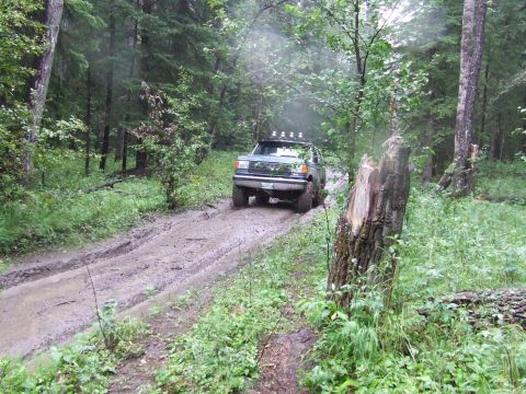 1990 Ford Bronco - 1990 Ford Bronco navigating a wet, muddy trail through a dense forest.