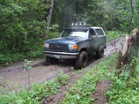 1990 Ford Bronco - This Ford Bronco navigates a muddy path in a forest, with rain visible in the air.
