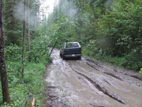 1990 Ford Bronco - Dark green 1990 Ford Bronco navigates a challenging muddy track through a dense forest.