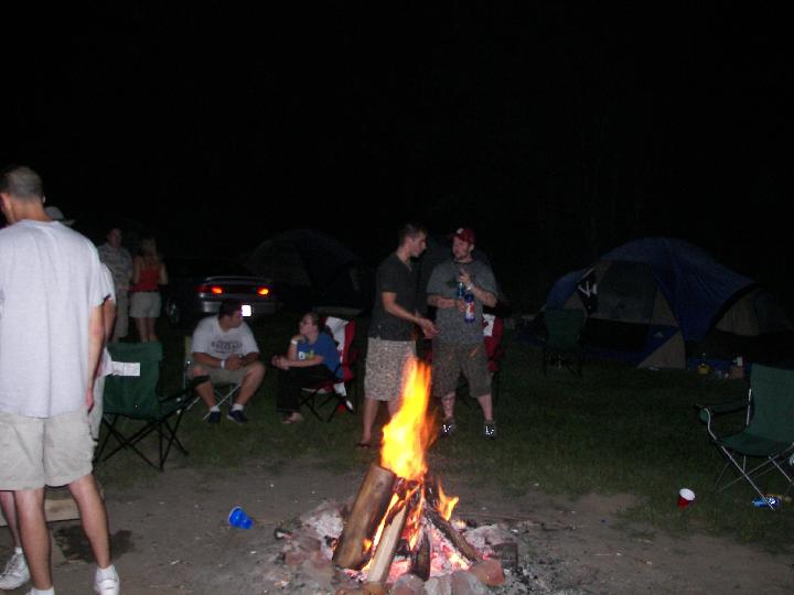People gathered around a campfire at night with tents set up in the background