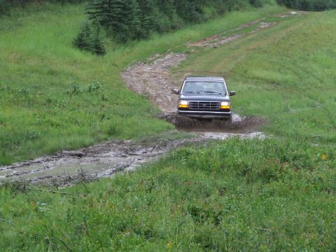 1990 Ford Bronco - Ford Econoline van navigating a challenging muddy off-road path.