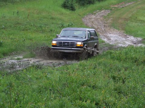 1990 Ford Bronco - This 1990 Ford Bronco is navigating a muddy trail, kicking up water as it goes.