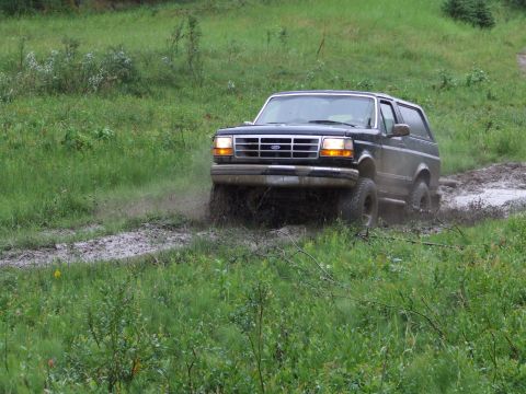 1990 Ford Bronco - A black Ford Bronco navigates a muddy track off-road.