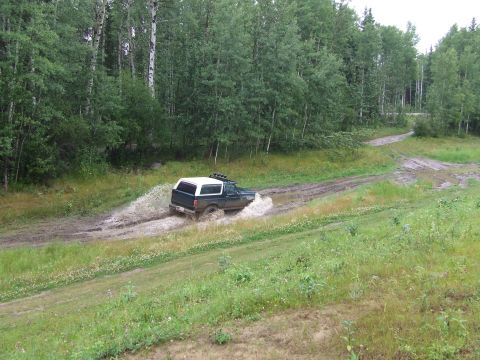 1990 Ford Bronco - A Ford Bronco navigates a wet and muddy off-road path, kicking up water as it goes.