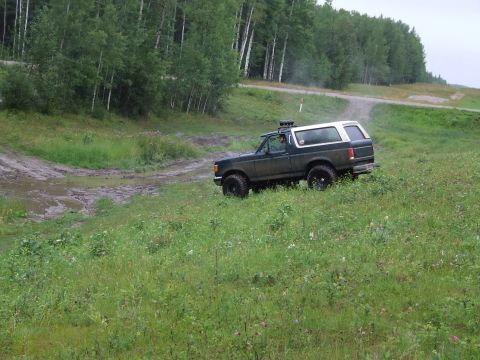 1990 Ford Bronco - A 1990 Ford Bronco navigates a muddy off-road course surrounded by trees and greenery.