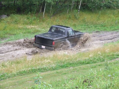 1990 Ford Bronco - Pickup truck navigating a challenging muddy terrain.