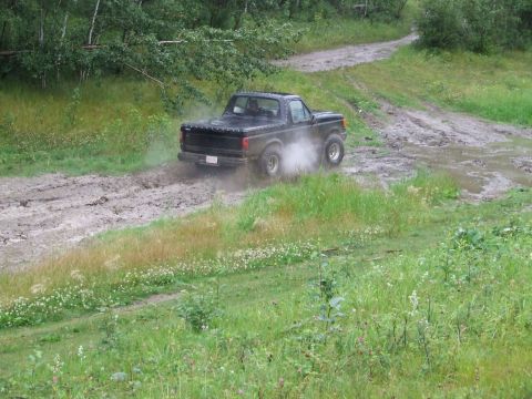1990 Ford Bronco - A black Ford Bronco navigates a muddy trail, kicking up dirt and dust.