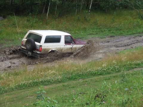 1990 Ford Bronco - This Ford Bronco is struggling to get through a muddy track, with water and mud splashing everywhere.