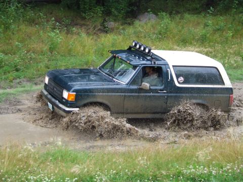 1990 Ford Bronco - A Ford Bronco navigates a muddy trail, splashing water as it goes.