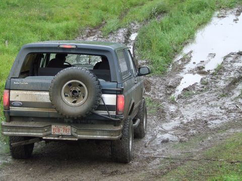 1990 Ford Bronco - Ford Bronco navigates a challenging muddy path with a spare tire on the back.