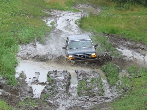 1990 Ford Bronco - Ford Bronco navigating a challenging muddy off-road path.