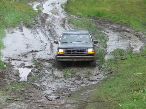 1990 Ford Bronco - A dark SUV, likely a 1992 Ford Bronco, struggles through a challenging muddy terrain.