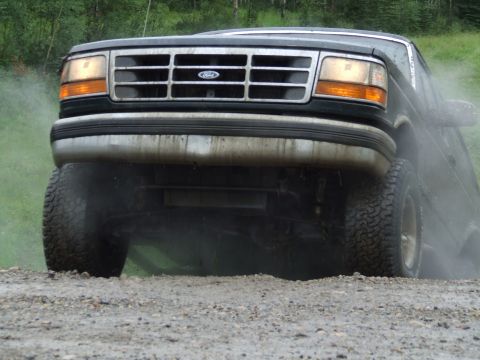 1990 Ford Bronco - Front view of a 1990 Ford Bronco kicking up dust on a gravel road.
