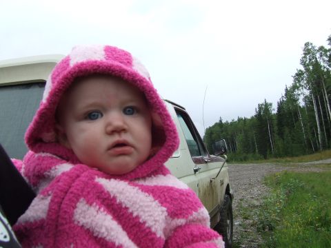 1990 Ford Bronco - A baby wearing a hooded jacket is in the passenger seat of a vehicle parked on a gravel road near a forest.