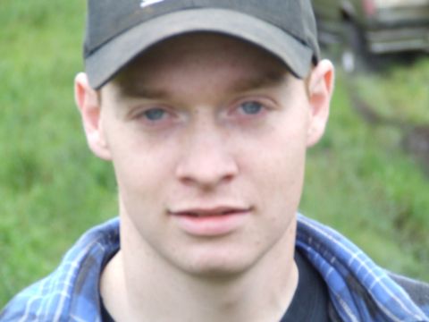 1990 Ford Bronco - A young man is shown from the chest up, wearing a baseball cap and a plaid shirt, with a blurred outdoor background.