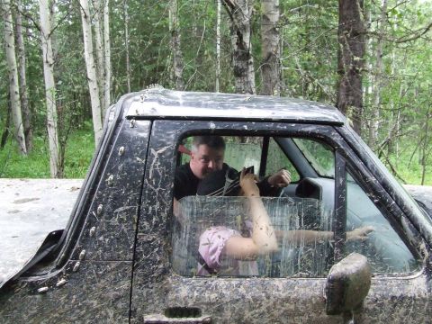 1990 Ford Bronco - Man and child inside a very muddy off-road vehicle, driving through a wooded area.