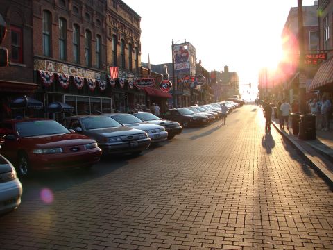 1992 Ford Taurus - A row of cars, including a red 1992 Ford Taurus, are parked along a brick-paved street lined with historic buildings.