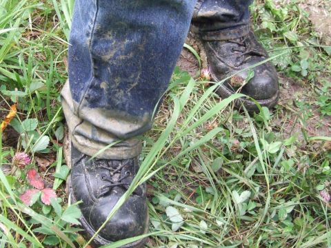 1990 Ford Bronco - A person wearing muddy jeans and boots stands in a grassy, dirt-covered area.