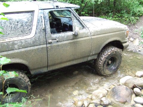 1990 Ford Bronco - This Ford Bronco is covered in mud as it drives through a rocky stream.
