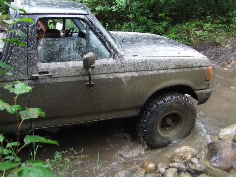1990 Ford Bronco - This truck is covered in mud as it navigates a rocky stream bed.