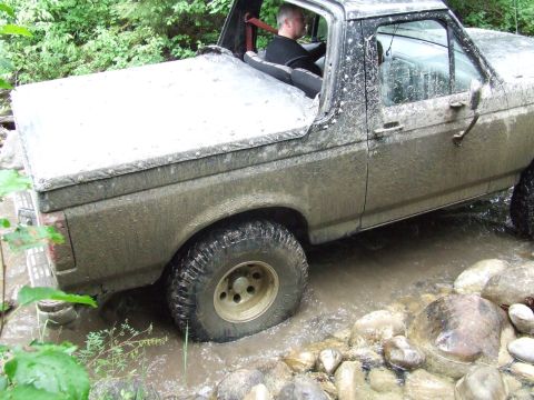 1990 Ford Bronco - A driver navigates a muddy Ford Bronco through a rocky stream.