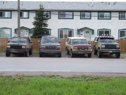 1990 Ford Bronco - Several SUVs are parked in front of a row of townhouses on a cloudy day.