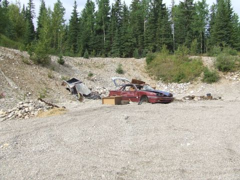 1990 Ford Bronco - Two heavily damaged vehicles sit abandoned in a wooded junkyard area.