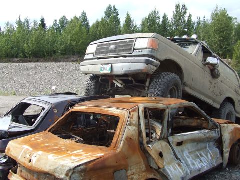 1990 Ford Bronco - A lifted 1990 Ford F-Series truck is parked on top of two heavily damaged and rusted cars.
