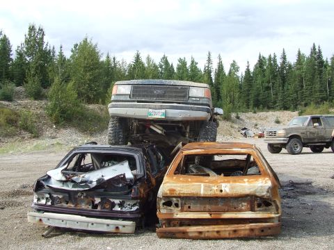 1990 Ford Bronco - A collection of wrecked vehicles, including a lifted truck and a Ford Bronco, in an outdoor junkyard setting.