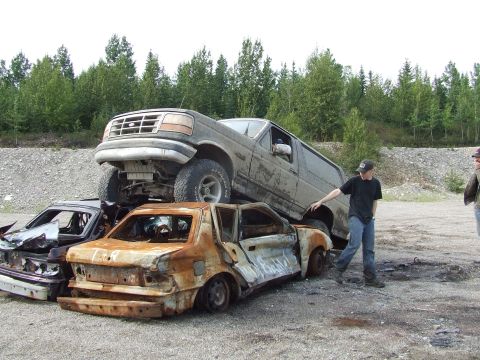 1990 Ford Bronco - A Ford Bronco is parked on top of two heavily damaged cars in a junkyard setting.